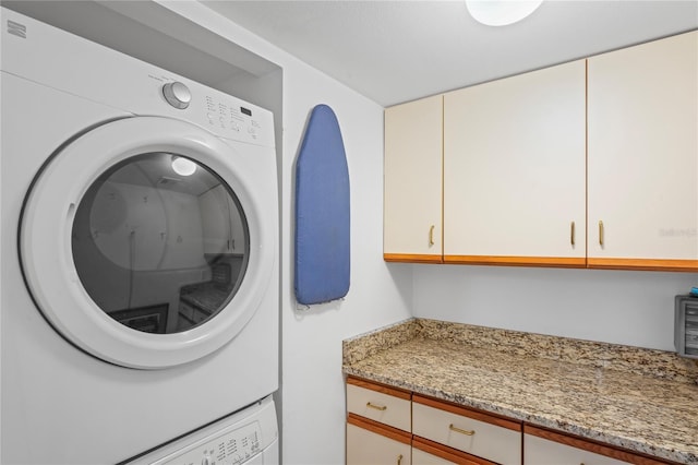 clothes washing area featuring cabinets and stacked washer / dryer