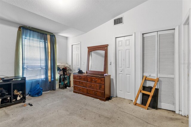 bedroom with multiple closets, carpet floors, a textured ceiling, and lofted ceiling