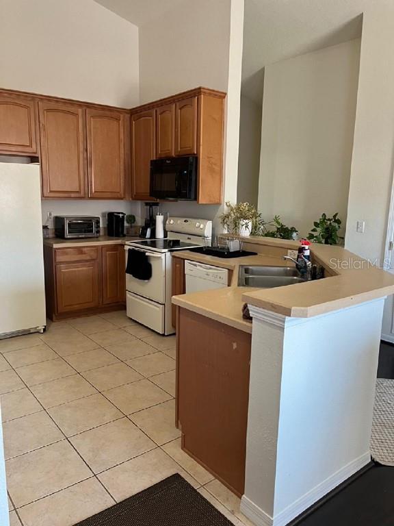 kitchen featuring kitchen peninsula, white appliances, sink, light tile patterned floors, and high vaulted ceiling