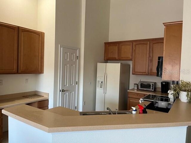 kitchen with kitchen peninsula, stainless steel fridge, and a towering ceiling