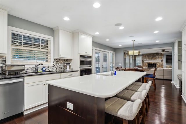 kitchen featuring appliances with stainless steel finishes, ceiling fan, a fireplace, a kitchen island, and hanging light fixtures