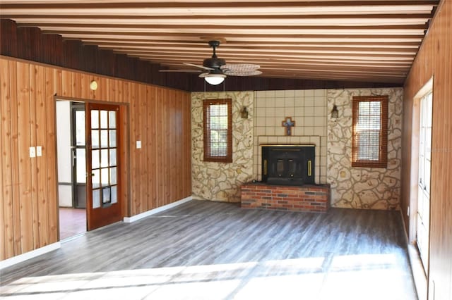 unfurnished living room featuring ceiling fan, a healthy amount of sunlight, hardwood / wood-style flooring, and a wood stove