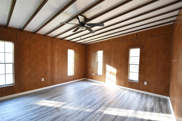 spare room with vaulted ceiling with beams, wood walls, wood-type flooring, and a healthy amount of sunlight