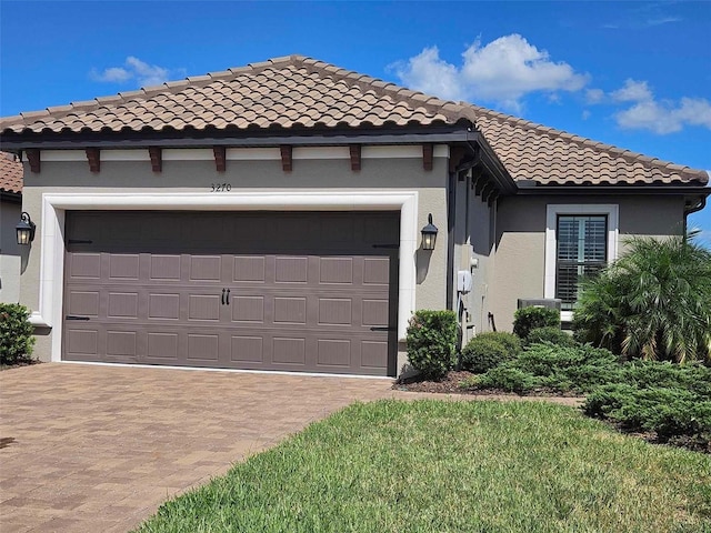 mediterranean / spanish-style home featuring stucco siding, a tile roof, decorative driveway, and a garage