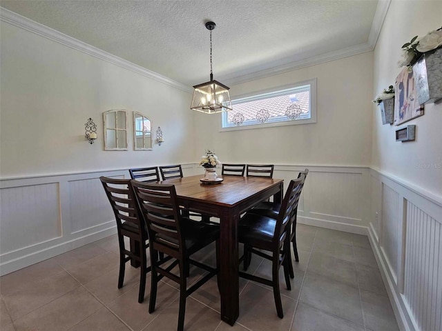 tiled dining space with ornamental molding, a textured ceiling, and an inviting chandelier