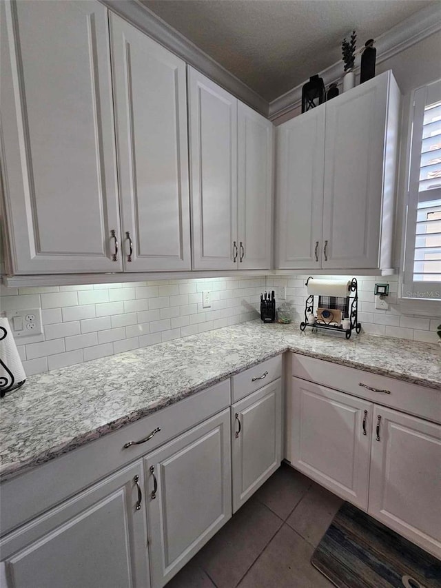 kitchen featuring backsplash, dark tile patterned flooring, crown molding, light stone countertops, and white cabinetry