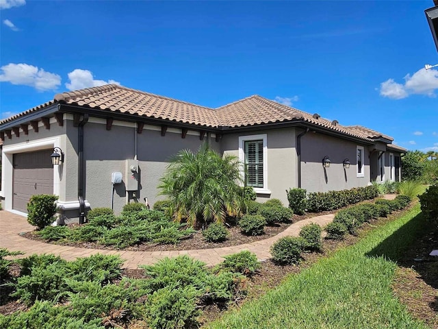 view of side of home with a tile roof, a garage, driveway, and stucco siding