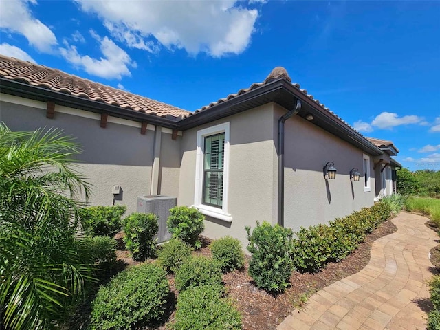 view of property exterior featuring stucco siding, central AC, and a tiled roof