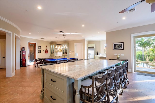 kitchen featuring billiards, light tile floors, light stone counters, a kitchen island, and crown molding