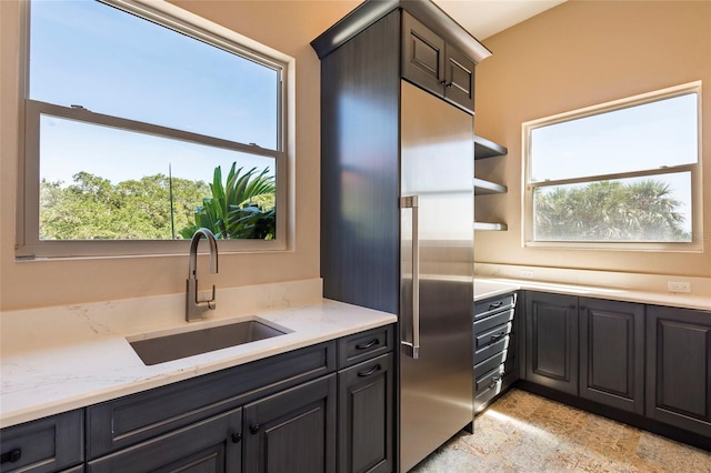 kitchen featuring stainless steel built in refrigerator, sink, light tile floors, and light stone counters