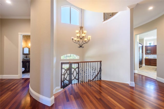 hallway featuring a notable chandelier, crown molding, dark hardwood / wood-style flooring, and a towering ceiling