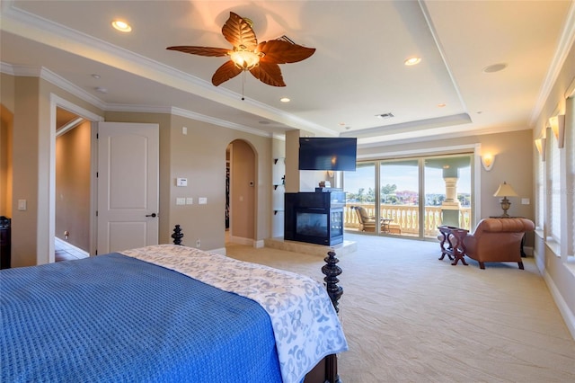 carpeted bedroom featuring ceiling fan, ornamental molding, a multi sided fireplace, a raised ceiling, and access to outside