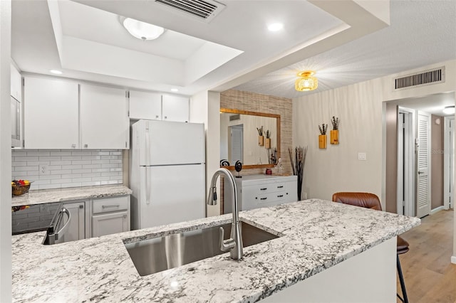 kitchen with sink, a kitchen breakfast bar, white refrigerator, kitchen peninsula, and a raised ceiling