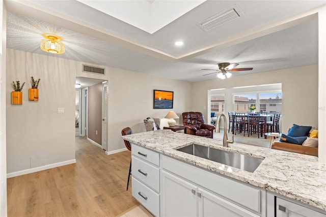 kitchen with sink, light hardwood / wood-style flooring, light stone countertops, and white cabinets