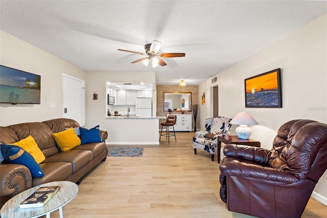 living room with ceiling fan, light hardwood / wood-style flooring, sink, and a textured ceiling