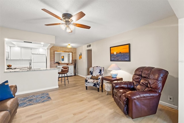 living room featuring ceiling fan, sink, light hardwood / wood-style floors, and a textured ceiling