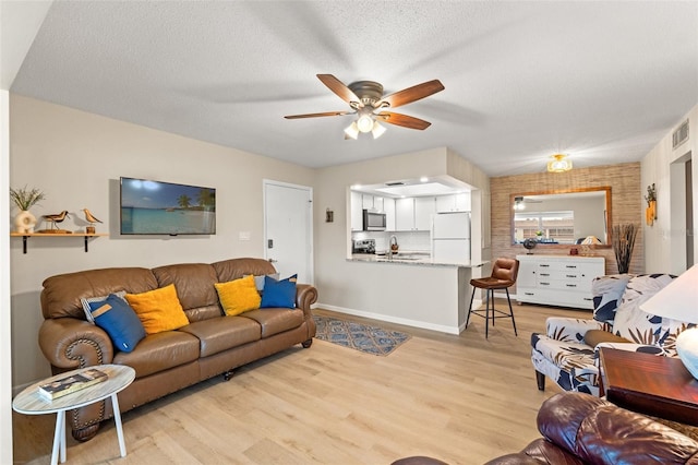 living room featuring ceiling fan, light hardwood / wood-style flooring, and a textured ceiling