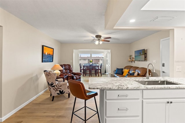 kitchen featuring sink, a breakfast bar area, white cabinetry, light stone counters, and light wood-type flooring