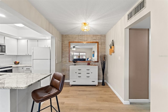 kitchen featuring white refrigerator, light stone countertops, white cabinets, a kitchen bar, and decorative backsplash