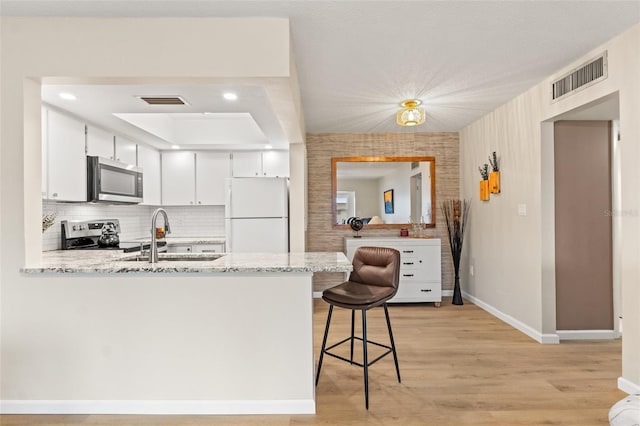 kitchen with appliances with stainless steel finishes, white cabinetry, a breakfast bar area, light stone counters, and kitchen peninsula