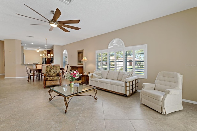 living room with a textured ceiling, light tile floors, and ceiling fan with notable chandelier