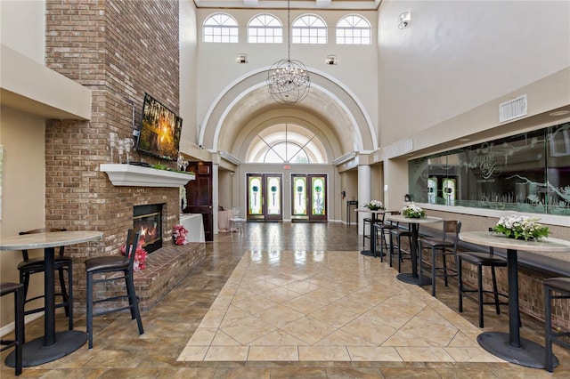 tiled foyer featuring a high ceiling, french doors, a brick fireplace, and an inviting chandelier