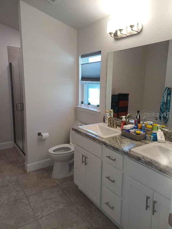 bathroom featuring double sink vanity, tile floors, toilet, and walk in shower