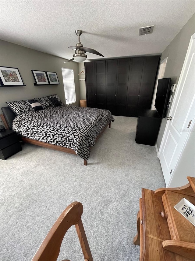 bedroom featuring a textured ceiling, light colored carpet, and ceiling fan