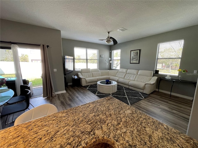 living room featuring plenty of natural light, dark hardwood / wood-style flooring, a textured ceiling, and ceiling fan