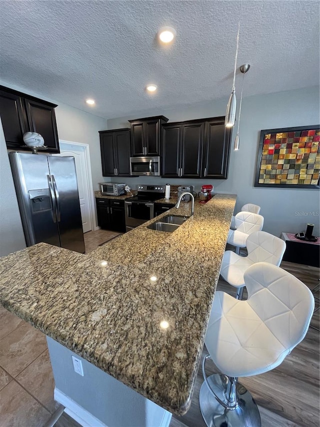 kitchen with stone countertops, a breakfast bar, appliances with stainless steel finishes, light wood-type flooring, and sink