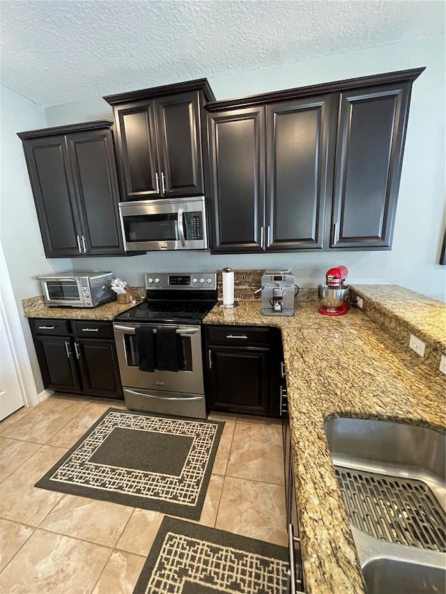 kitchen featuring sink, light stone counters, stainless steel appliances, light tile flooring, and a textured ceiling