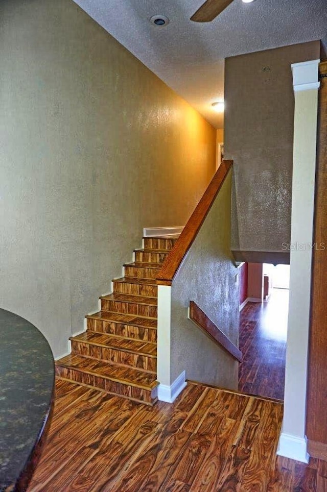 stairs featuring a textured ceiling, wood-type flooring, and ceiling fan