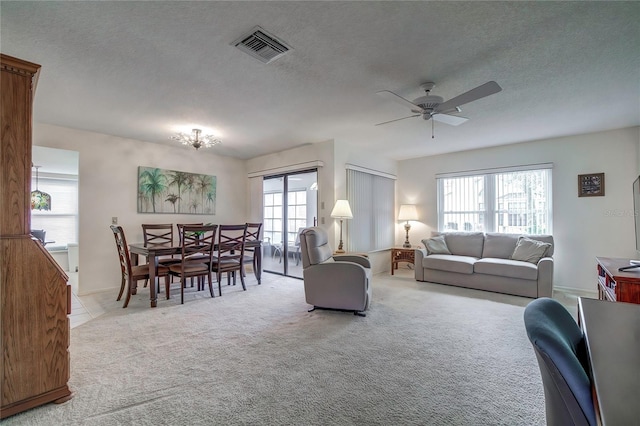 carpeted living room with a textured ceiling and ceiling fan with notable chandelier