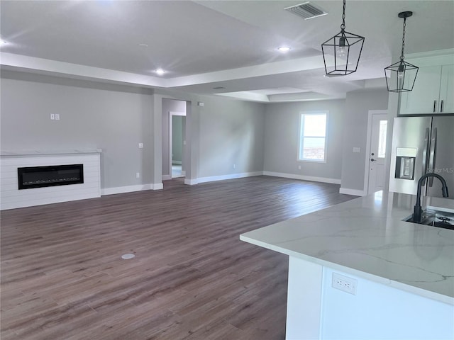 kitchen with sink, pendant lighting, light stone counters, stainless steel refrigerator with ice dispenser, and dark wood-type flooring