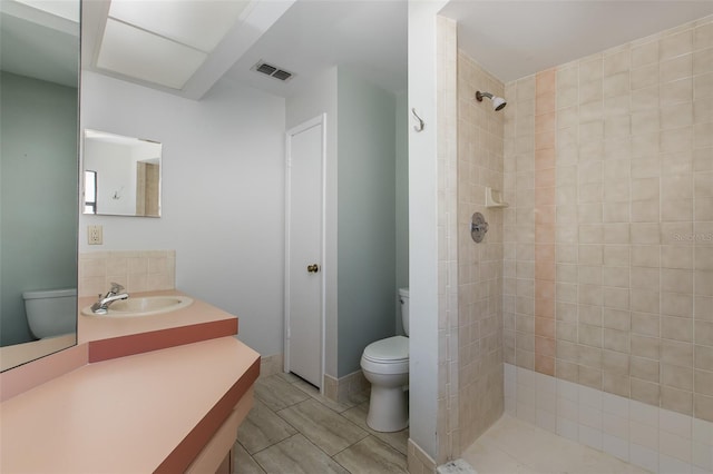 bathroom featuring toilet, vanity, tiled shower, and tile flooring