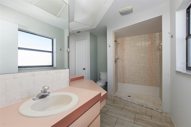 bathroom featuring vanity, tiled shower, tile flooring, toilet, and tasteful backsplash