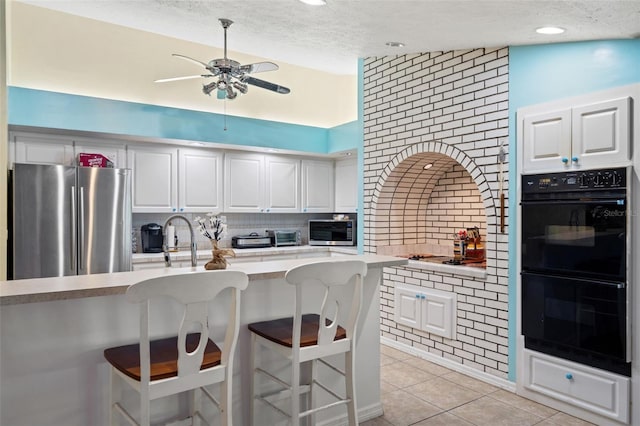 kitchen with backsplash, vaulted ceiling, a kitchen bar, white cabinets, and appliances with stainless steel finishes