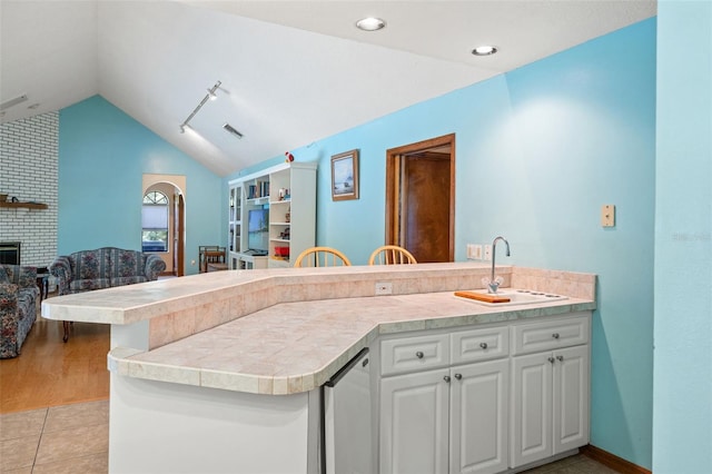 kitchen with kitchen peninsula, vaulted ceiling, white cabinetry, and sink