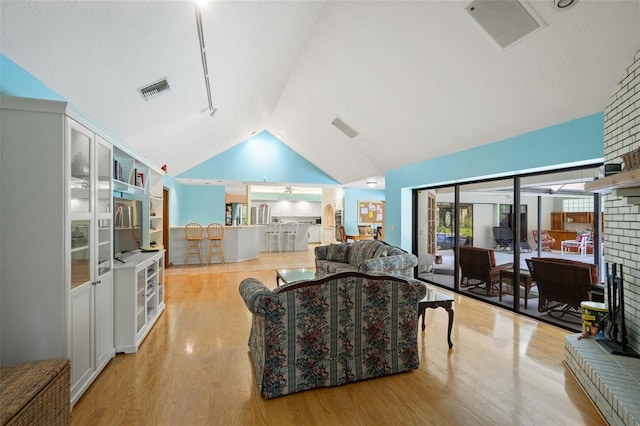 living room featuring light wood-type flooring, a brick fireplace, ceiling fan, and lofted ceiling