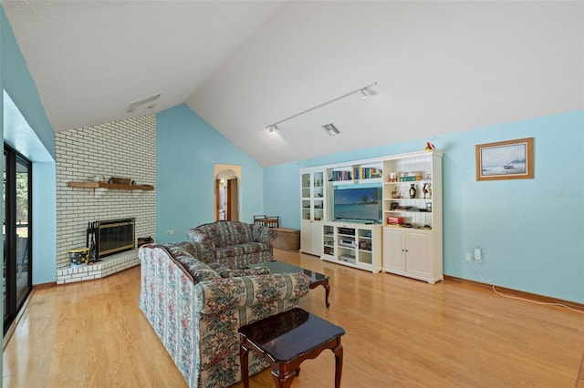 living room featuring built in shelves, vaulted ceiling, light hardwood / wood-style flooring, and a brick fireplace