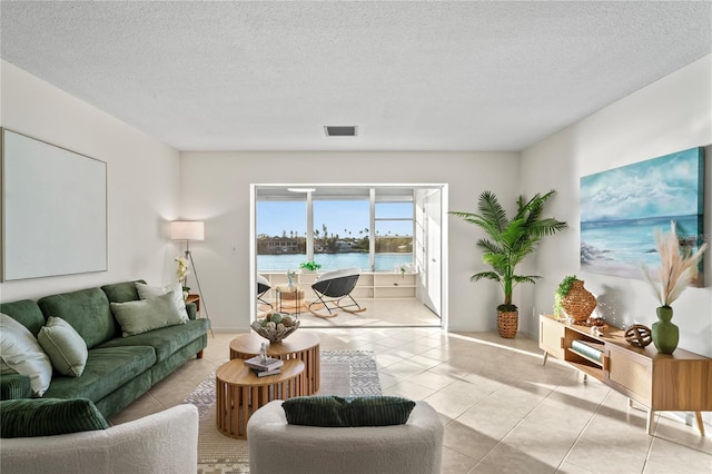 living area featuring visible vents, a water view, a textured ceiling, and light tile patterned floors