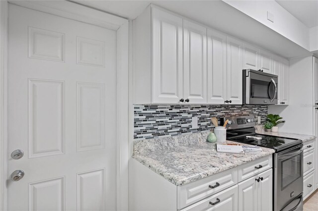 kitchen featuring white cabinets, light stone countertops, appliances with stainless steel finishes, and decorative backsplash