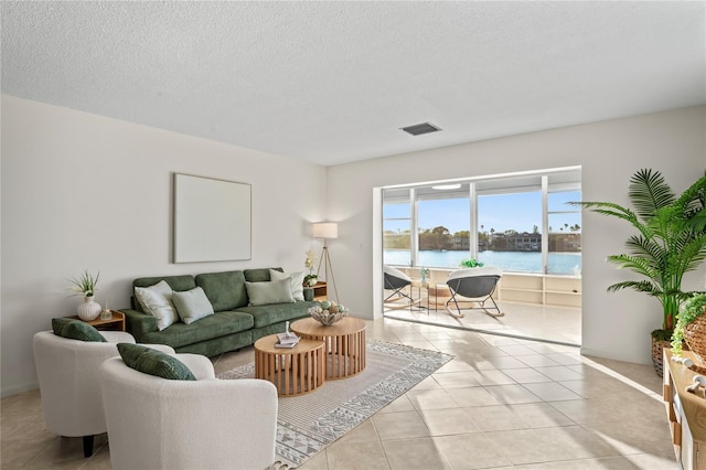 living room with visible vents, a water view, a textured ceiling, and tile patterned floors