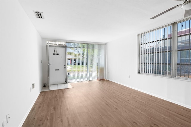 empty room featuring ceiling fan, expansive windows, wood-type flooring, and a wealth of natural light