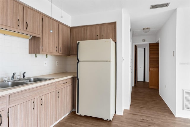 kitchen with backsplash, sink, white fridge, and wood-type flooring