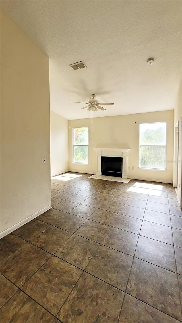 unfurnished living room featuring dark tile floors, a textured ceiling, and ceiling fan