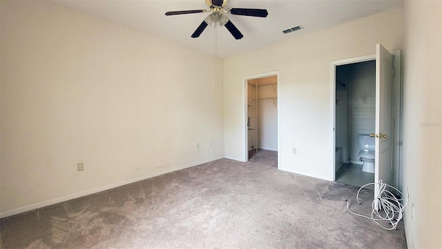 unfurnished bedroom featuring connected bathroom, a closet, ceiling fan, a walk in closet, and dark carpet