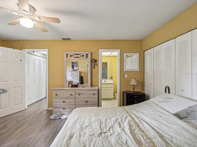 bedroom featuring ensuite bath, ceiling fan, hardwood / wood-style floors, and two closets