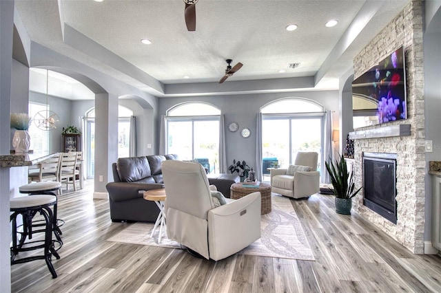 living room with a fireplace, light wood-type flooring, a textured ceiling, and ceiling fan with notable chandelier