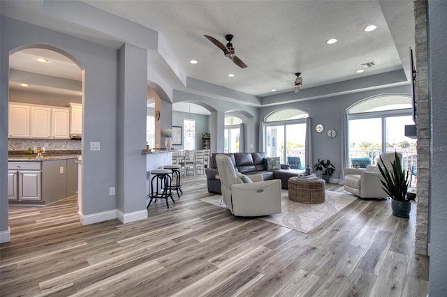 living area featuring a textured ceiling, a ceiling fan, visible vents, baseboards, and light wood-type flooring